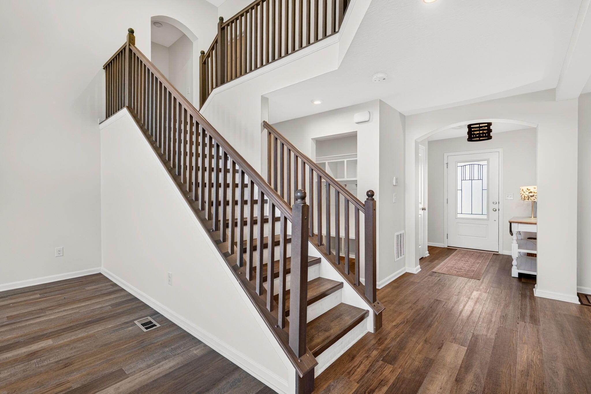 Two-story foyer with a dark wood staircase, arched entry, and decorative-glass front door.
