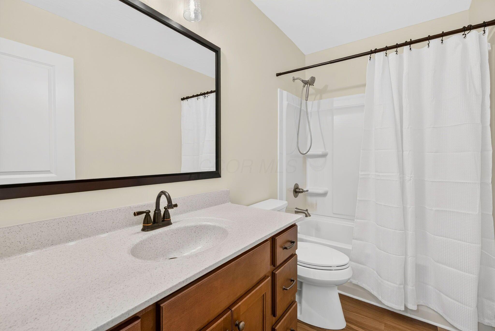 Bathroom with a speckled vanity, wood cabinets, and a white tub-shower behind a curtain.