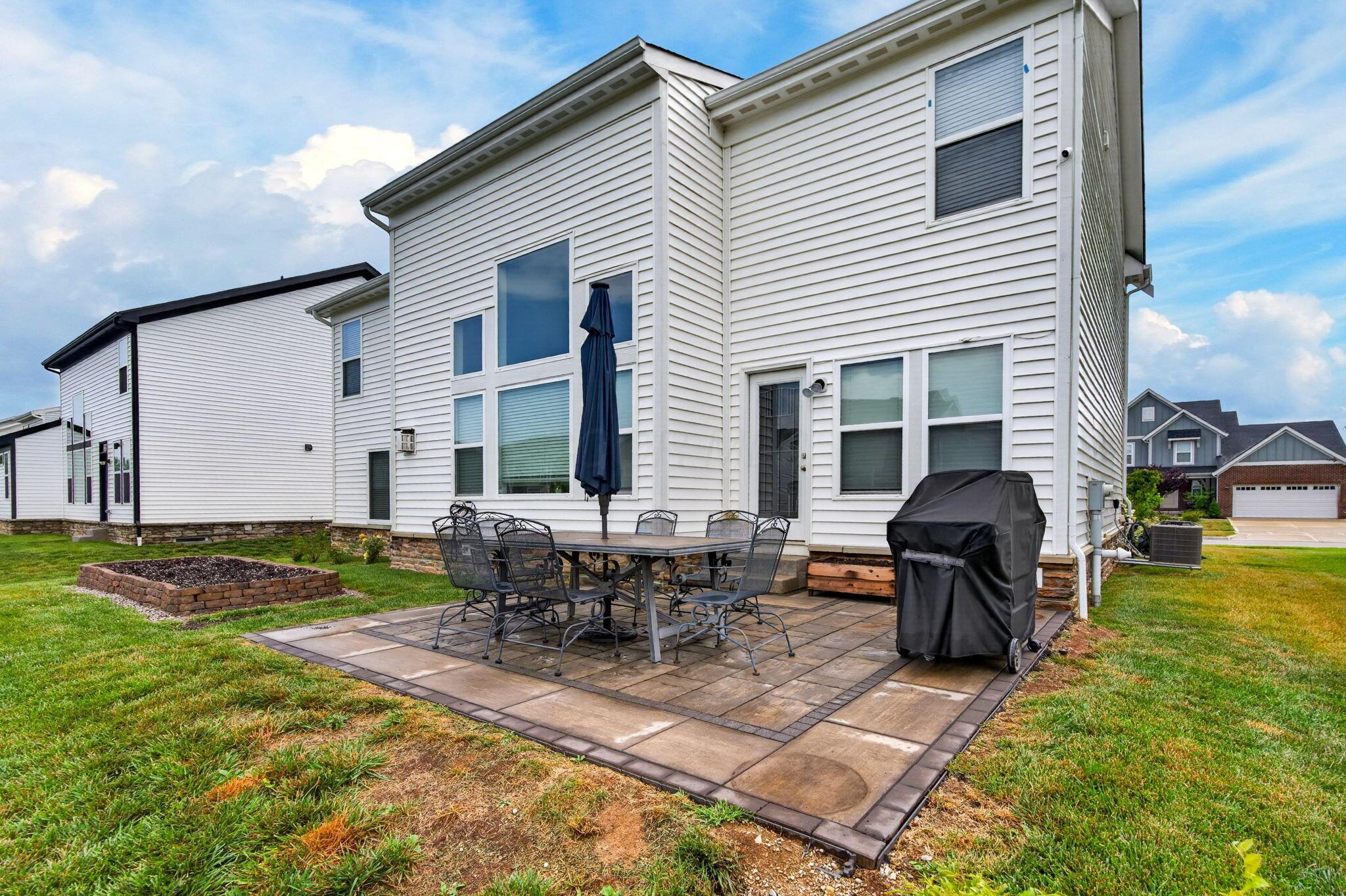 White two-story home with a paved backyard patio, outdoor dining set, and covered grill.