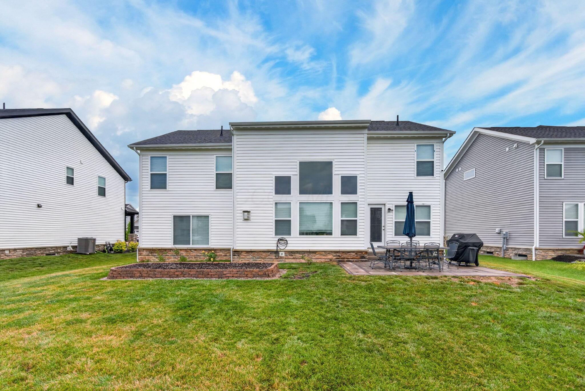 Rear of a white two-story home with a broad lawn, raised garden bed, and furnished patio.