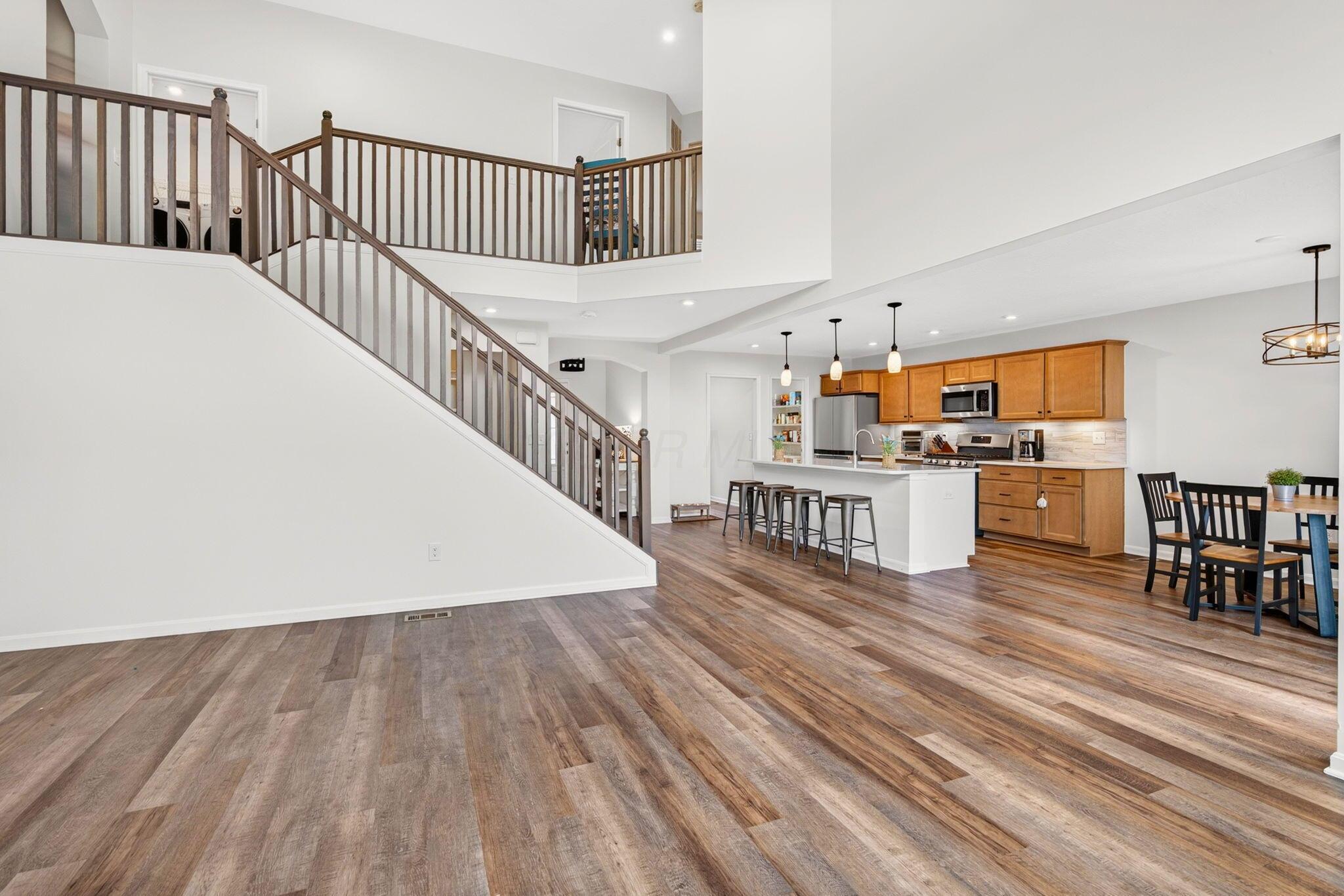 Open kitchen and dining area with a white island, warm wood cabinets, and a prominent staircase.