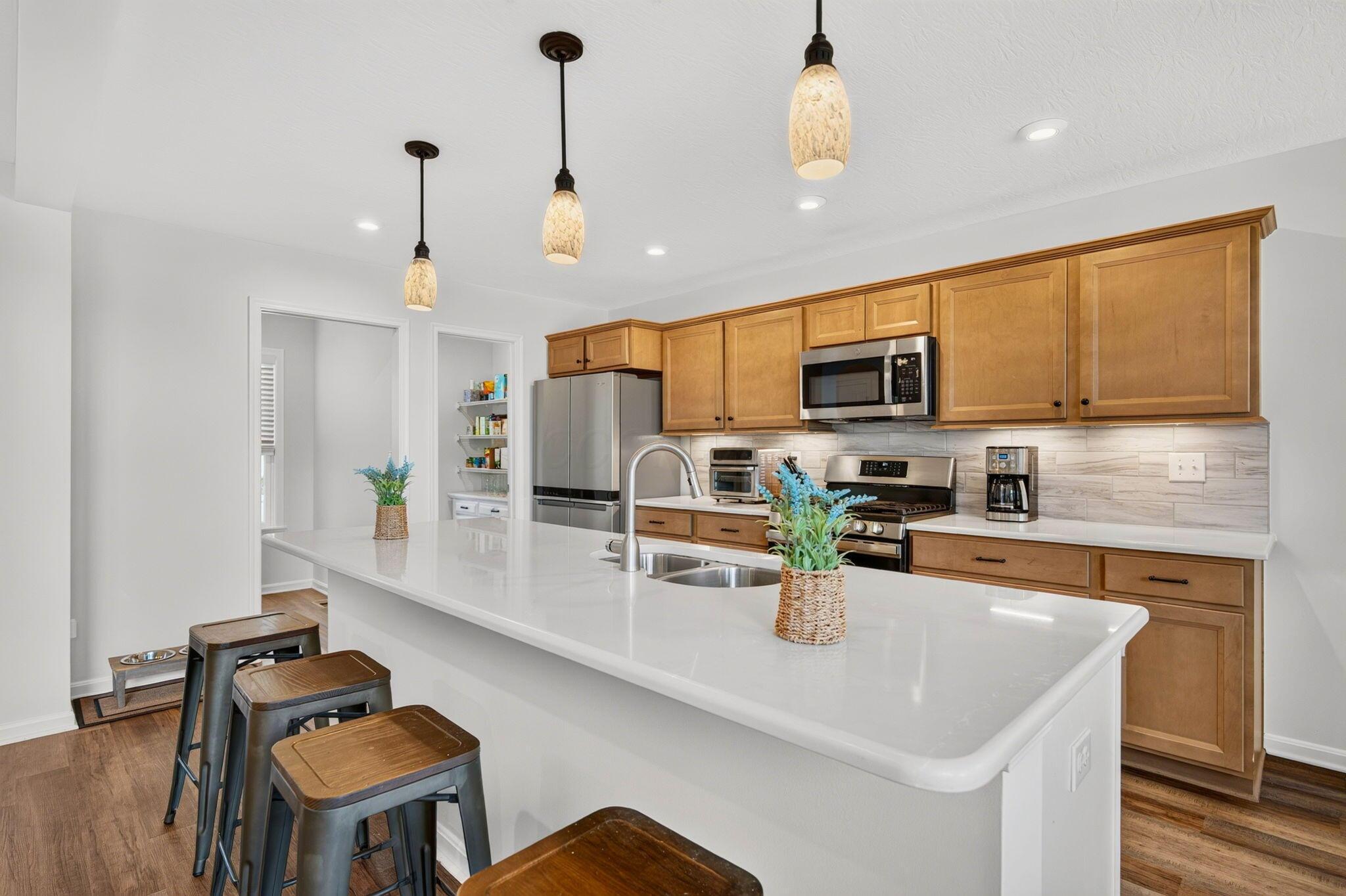 Kitchen with a large white island, warm wood cabinets, stainless steel appliances, and pendant lights.