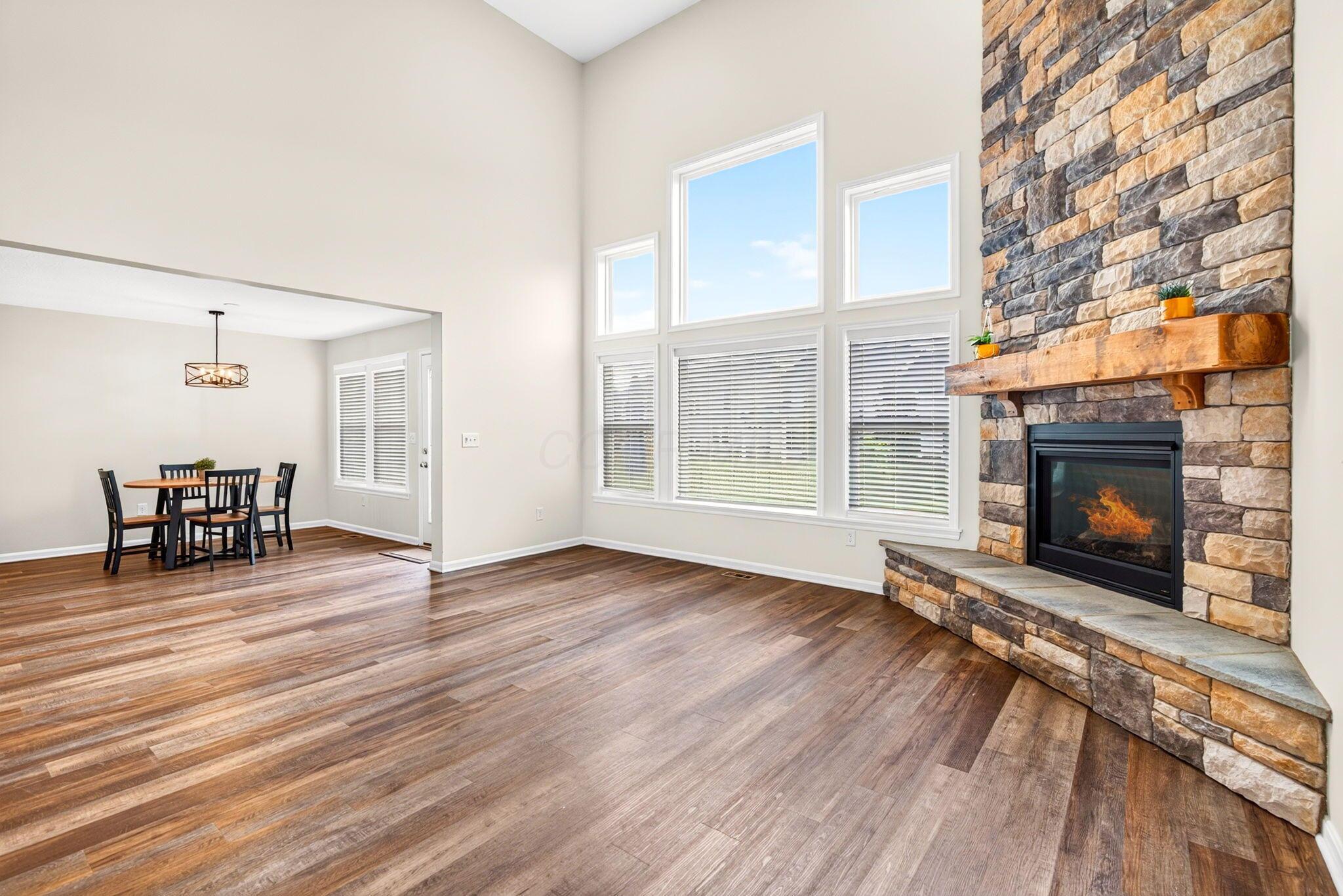 Living room with a floor-to-ceiling stone fireplace, tall windows, and adjoining dining area.