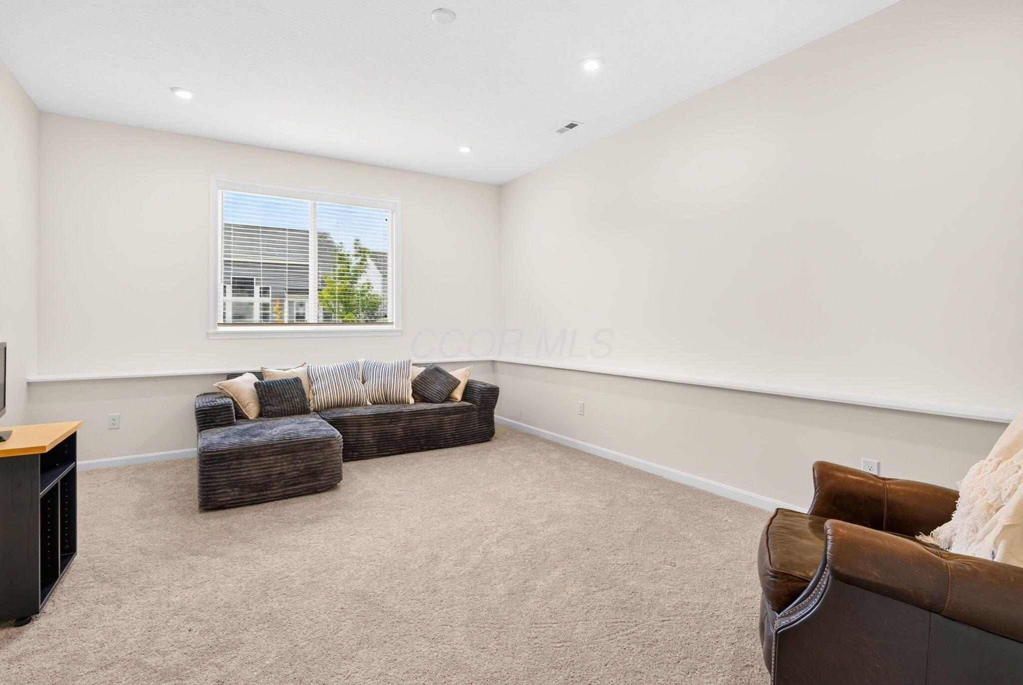 Furnished living room with a dark sectional sofa, beige carpet, and a brown leather armchair.