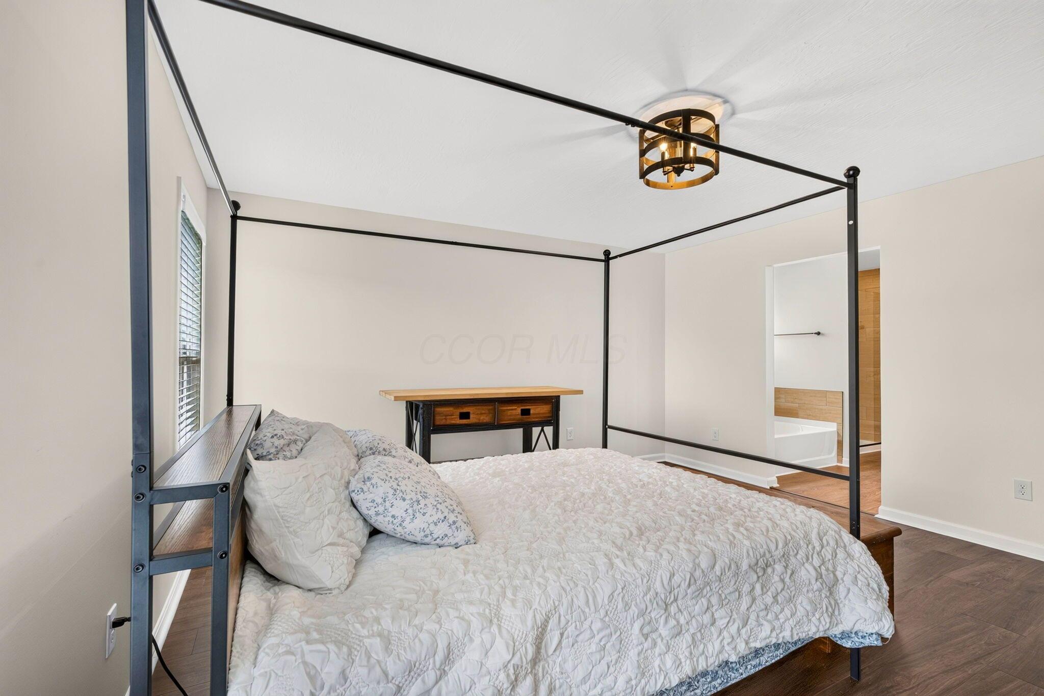 Bedroom with a black four-poster bed, white quilt, and doorway to an adjoining bathroom.