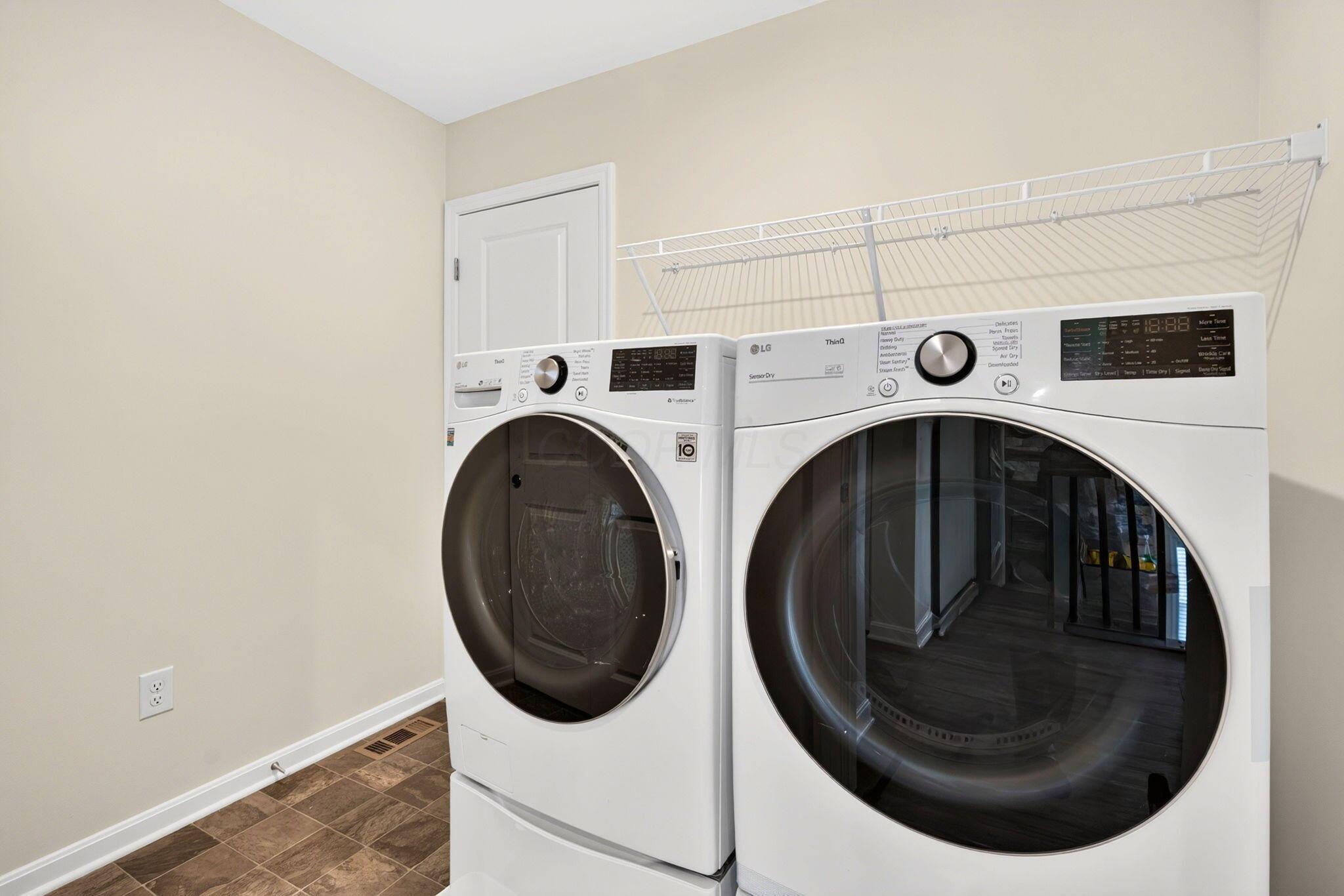 Laundry room with white front-loading washer and dryer beneath a wall-mounted drying rack.