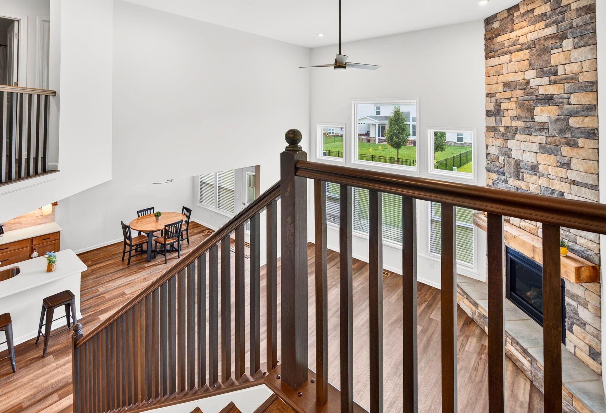 Upstairs landing overlooking an open living area, with dark wood railing, a stone fireplace, and hardwood floors.