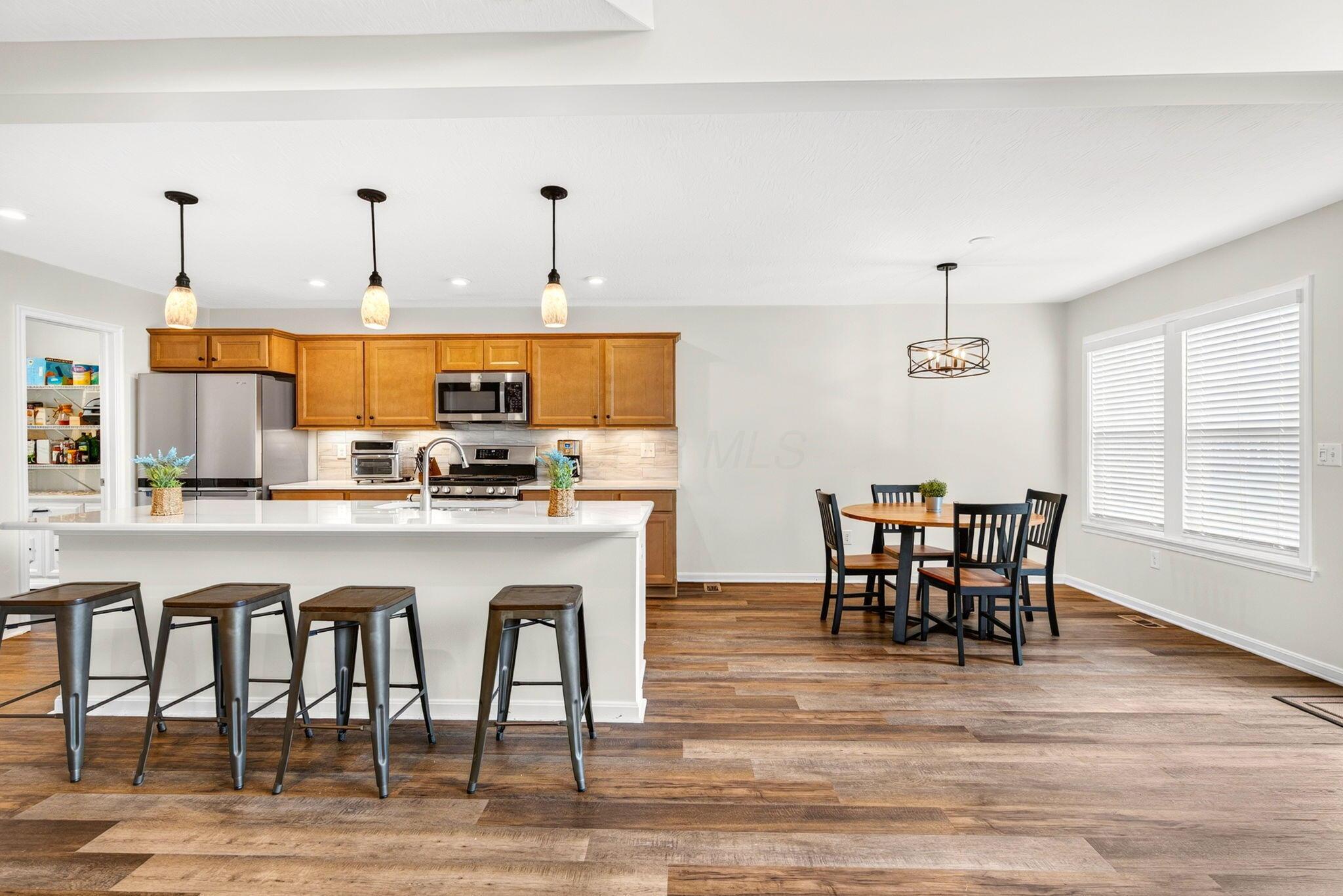 Open kitchen with wood cabinets and a white island adjoining a dining area with large windows.