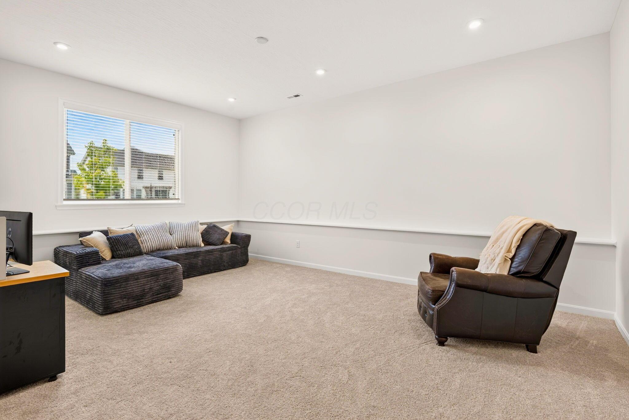 Furnished living room with a dark sectional, leather recliner, beige carpet, and large window.