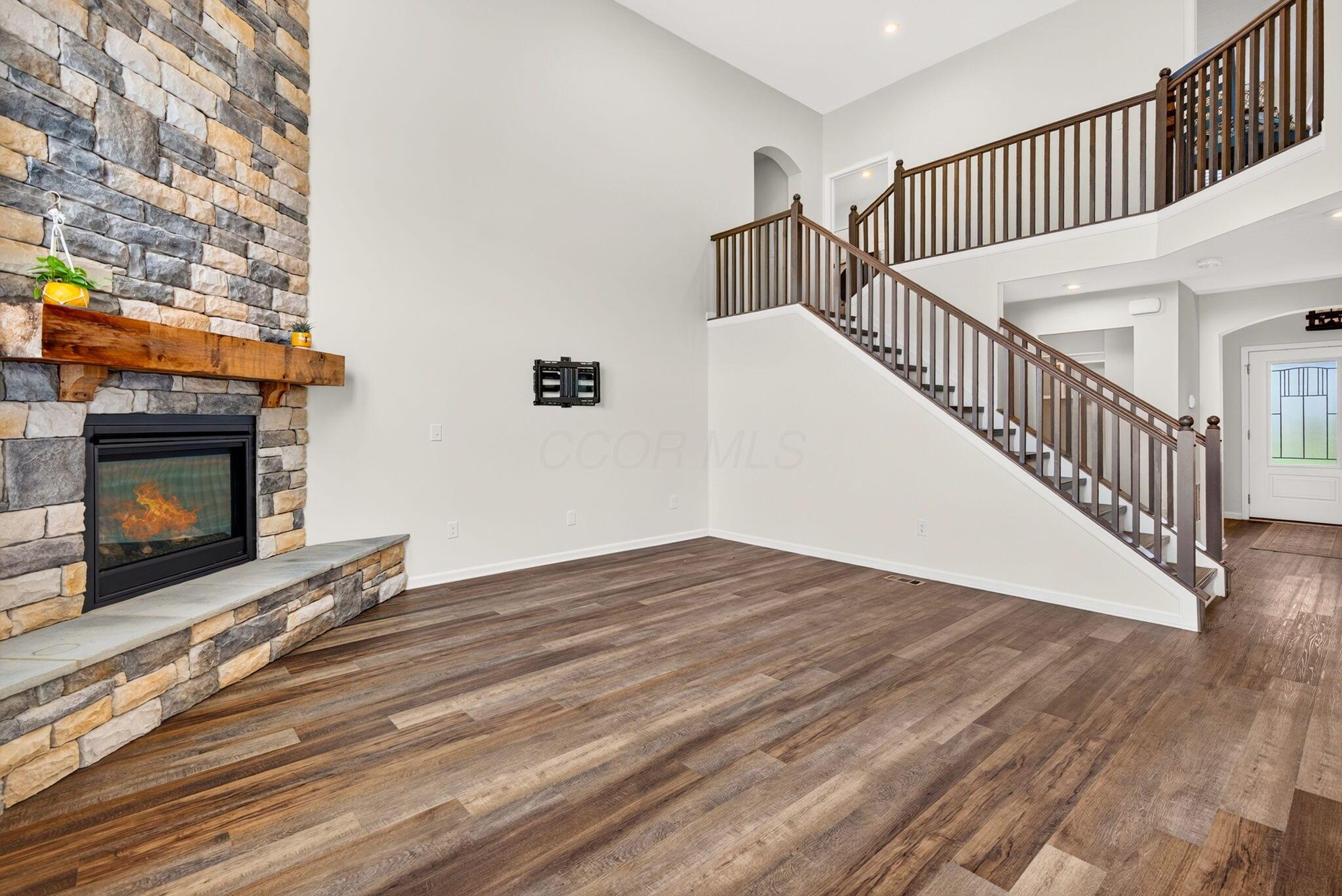 Living room with a stone fireplace, wide-plank flooring, and an open staircase.