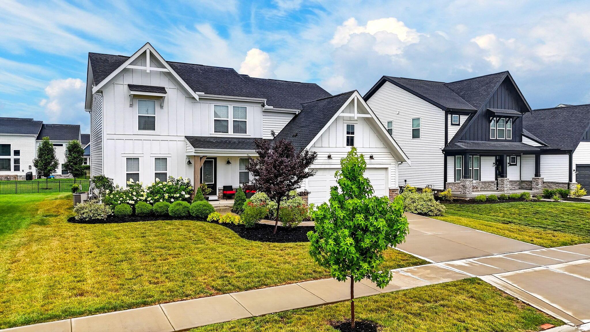 White two-story home with gabled roof, attached garage, and landscaped front lawn.
