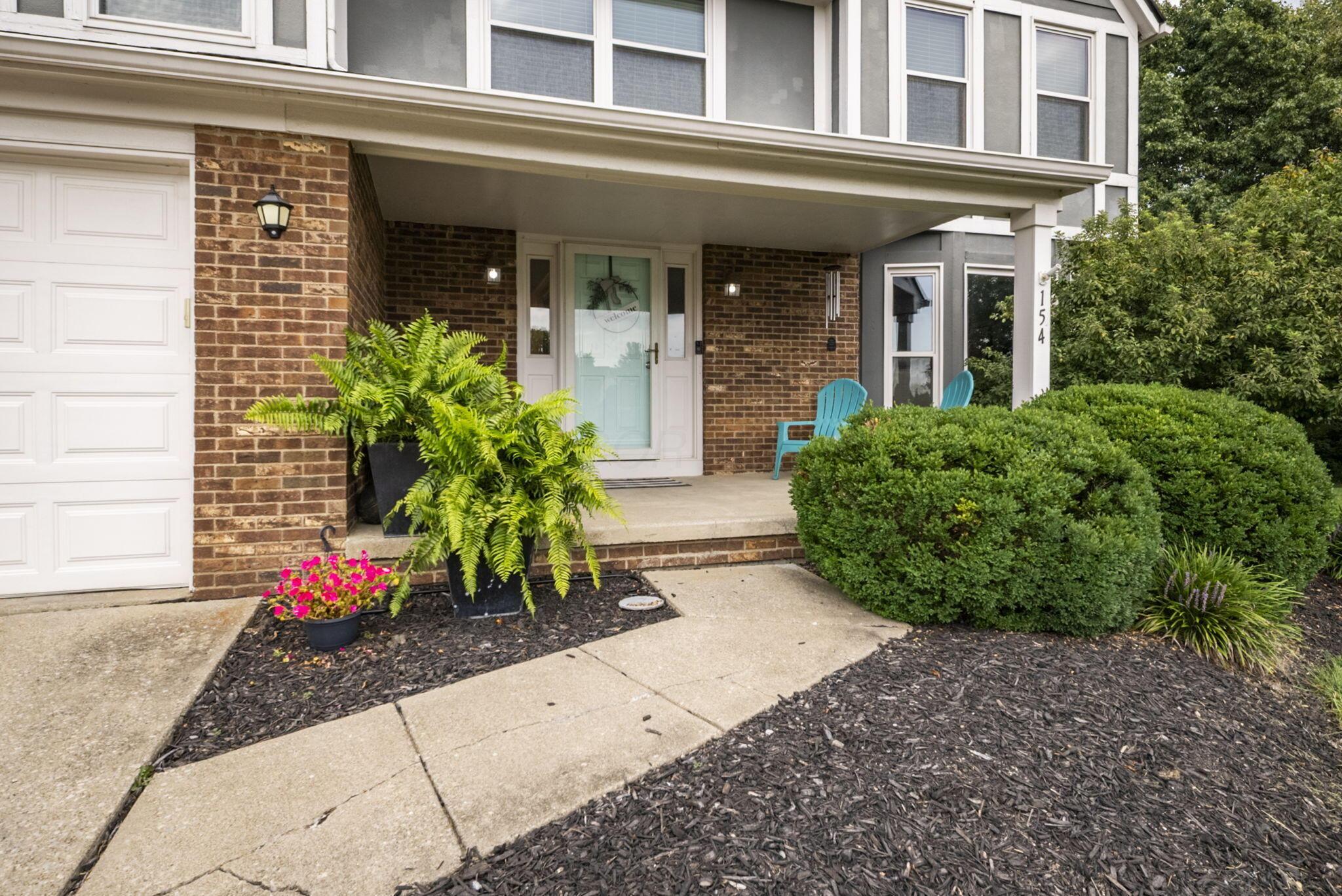 Front entrance with a covered porch, brick walls, turquoise chairs, and landscaped shrubs.
