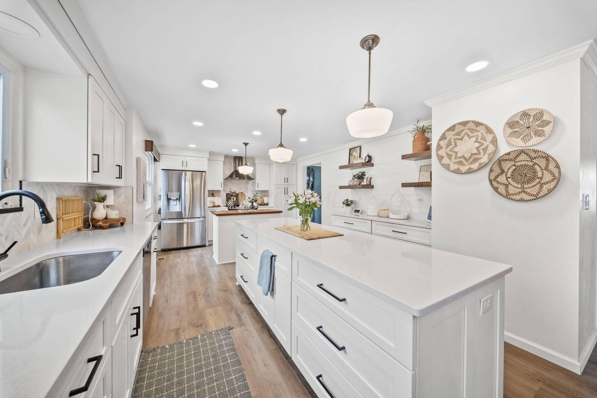 Bright white kitchen with a large island, stainless steel refrigerator, and farmhouse sink.