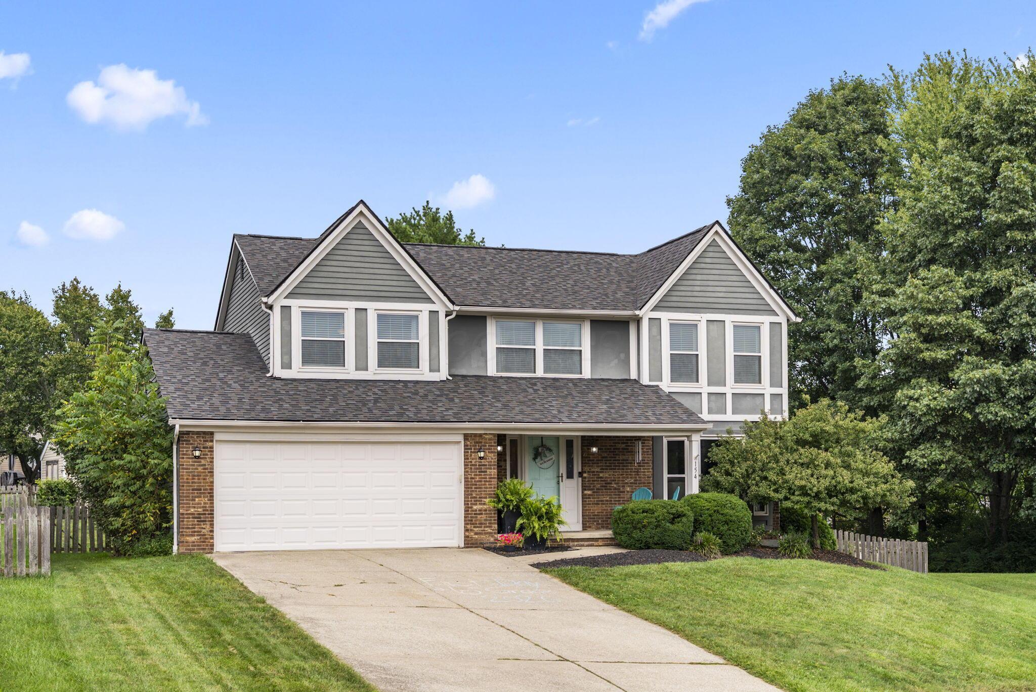 Two-story gray and brick house with a double garage, pale green door, and broad driveway.