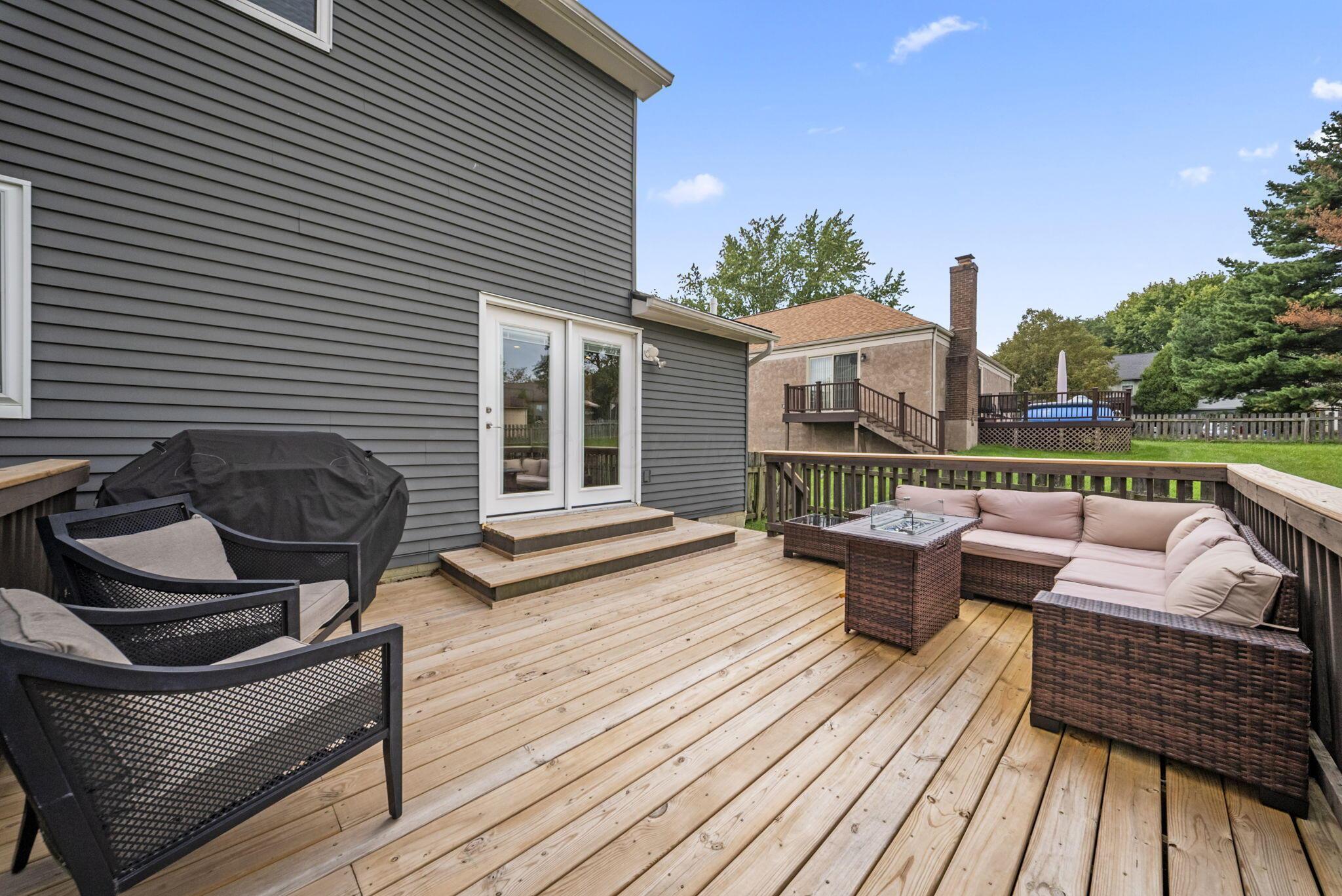 Backyard deck with a wicker sectional, armchairs, and covered grill beside a gray-sided house.