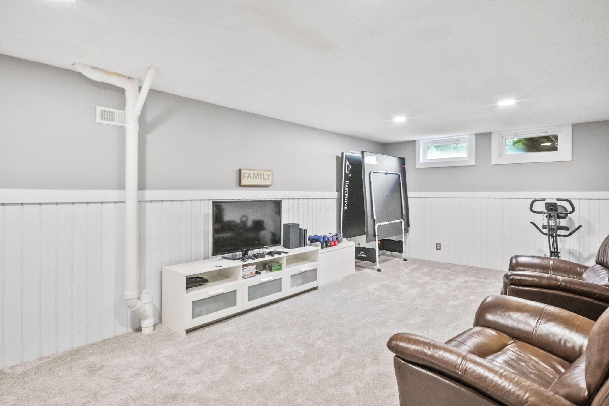 Finished basement recreation room with leather recliners, a TV, and exercise equipment.