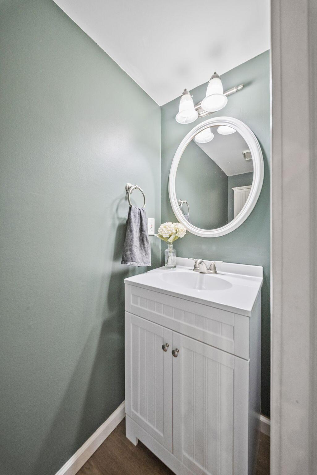 Bathroom vanity with sage-green walls, oval mirror, and gray towel.