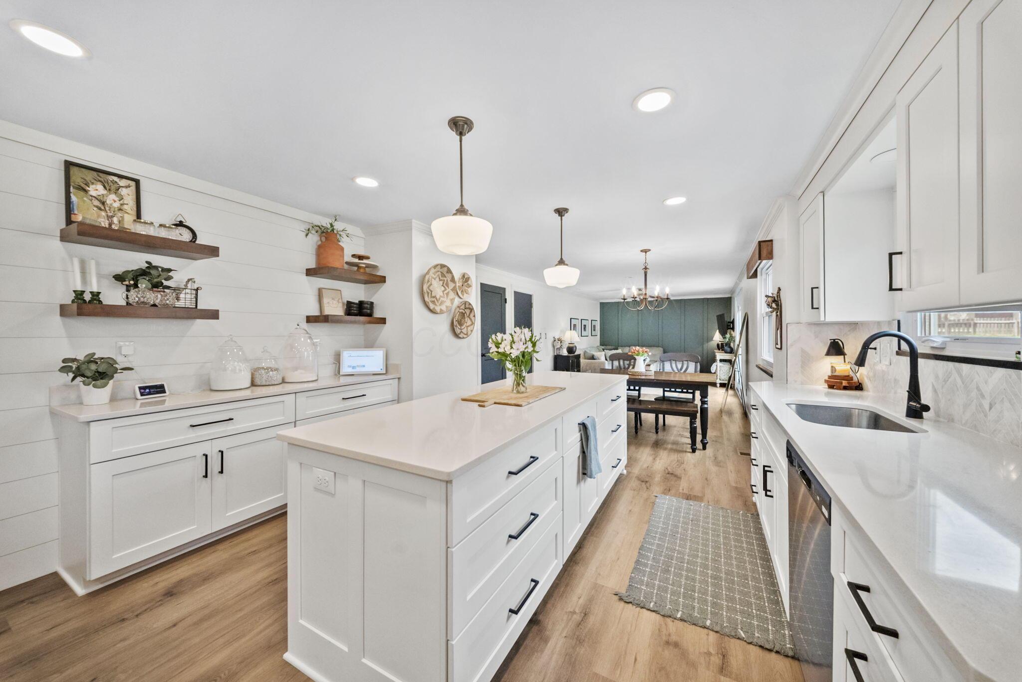 Bright white kitchen with a large island, open shelves, and views into the dining and living areas.