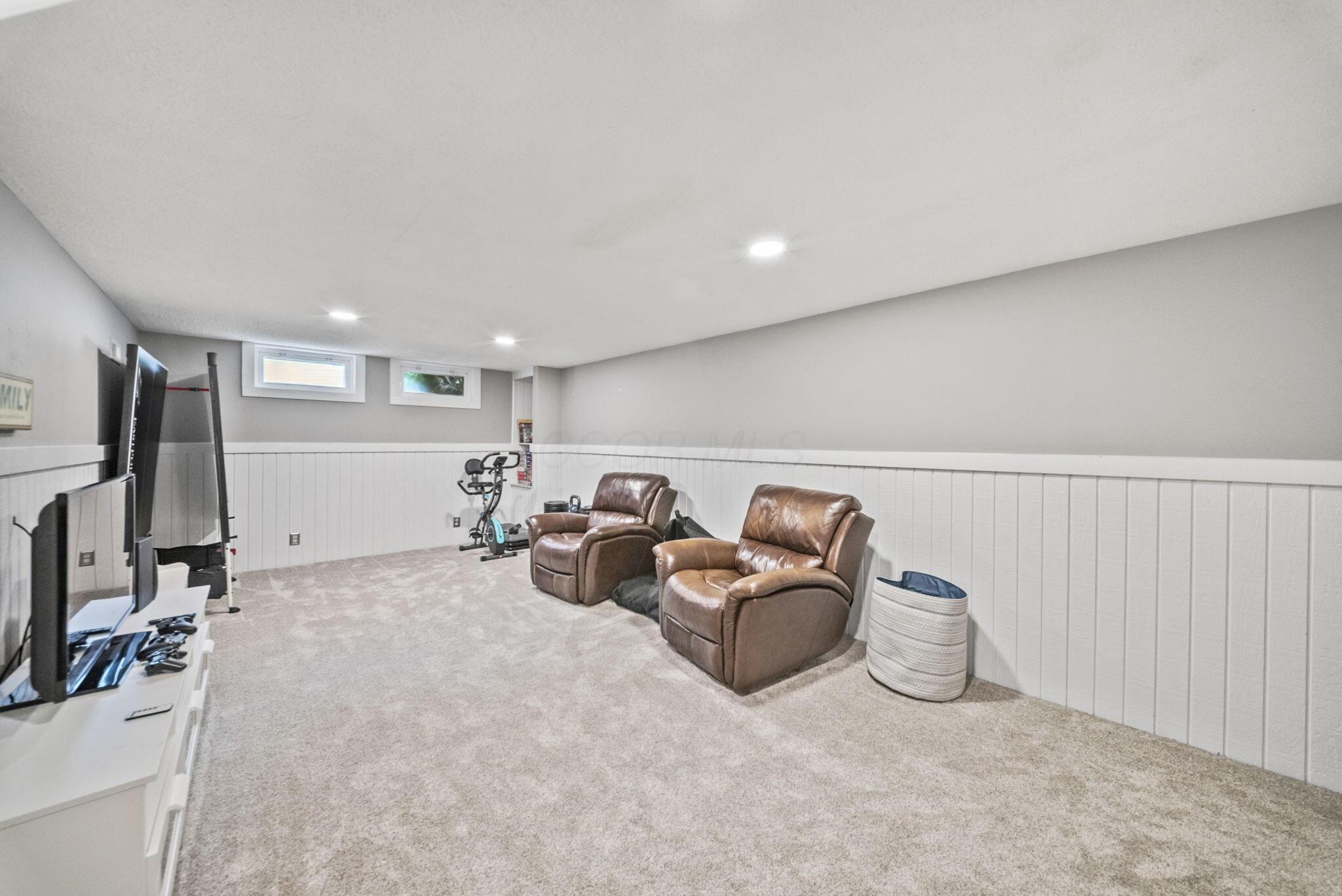 Basement recreation room with two brown leather recliners, a television, and exercise equipment.