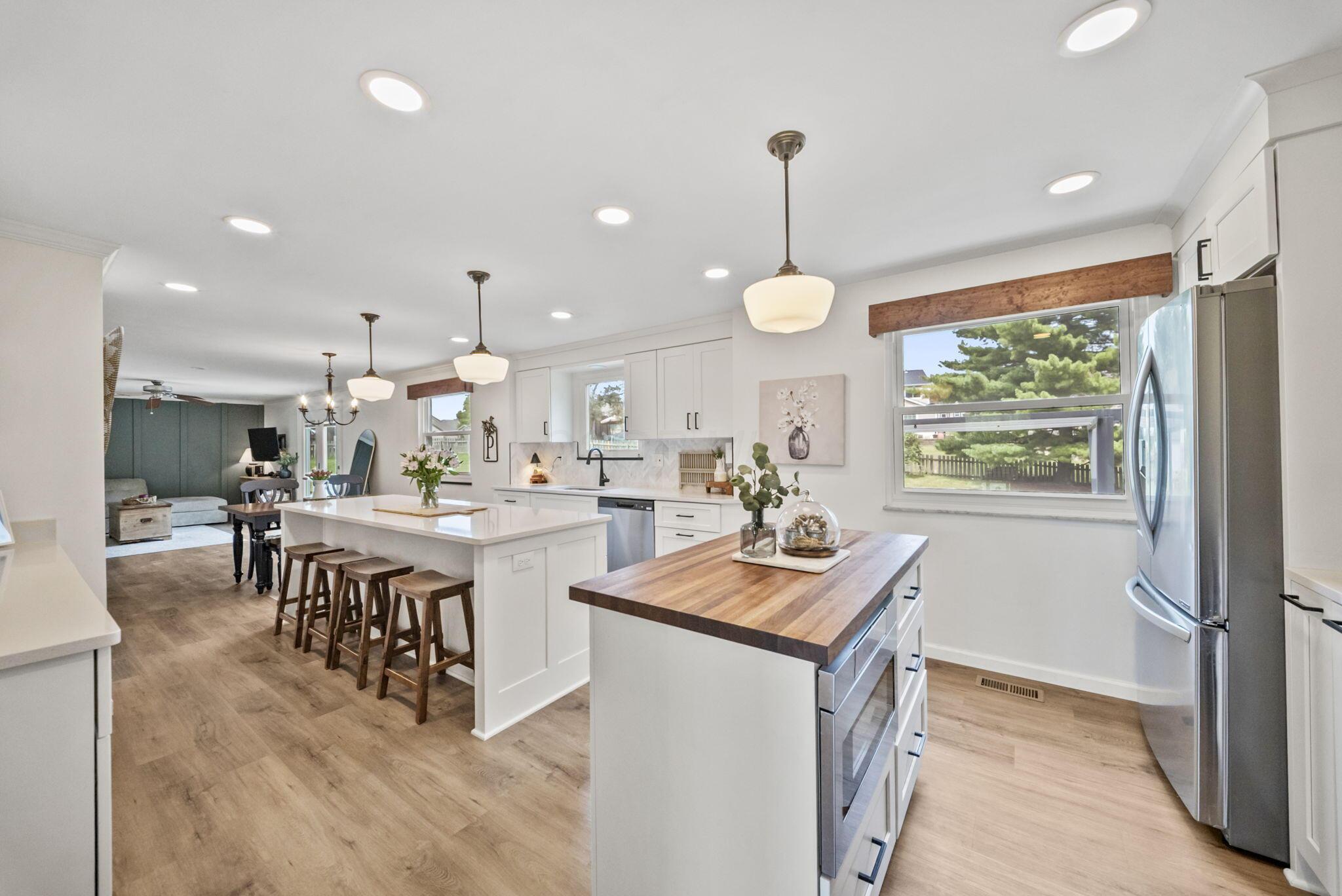 Open-plan kitchen with white cabinets, wood-topped islands, bar stools, and living area beyond.