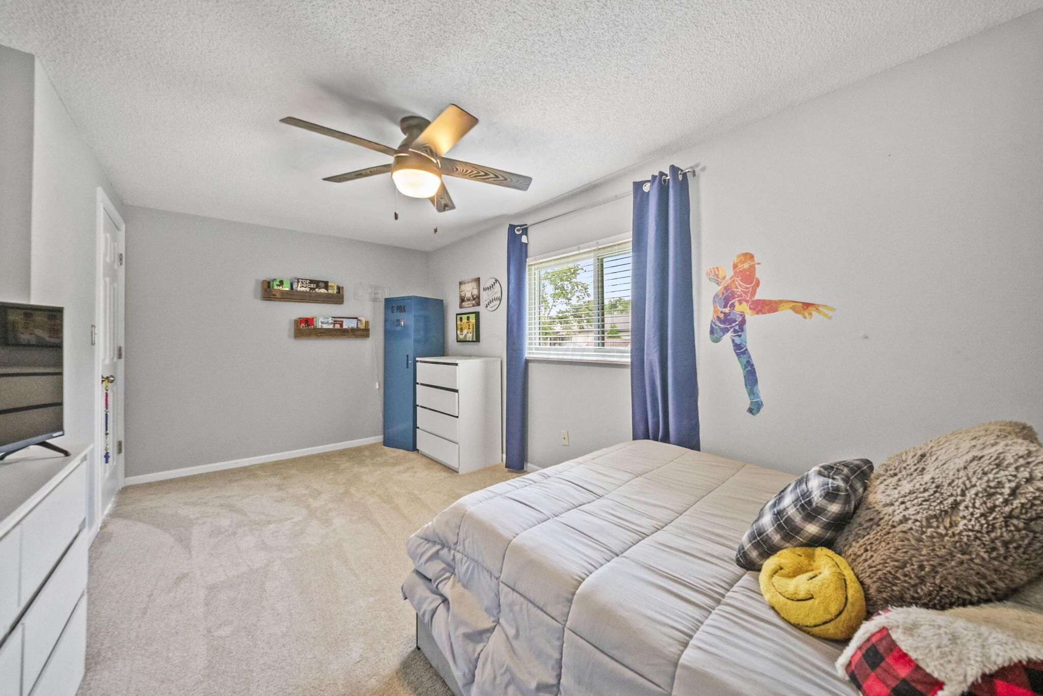Furnished bedroom with blue curtains, a blue wardrobe, and colorful baseball-player wall art.