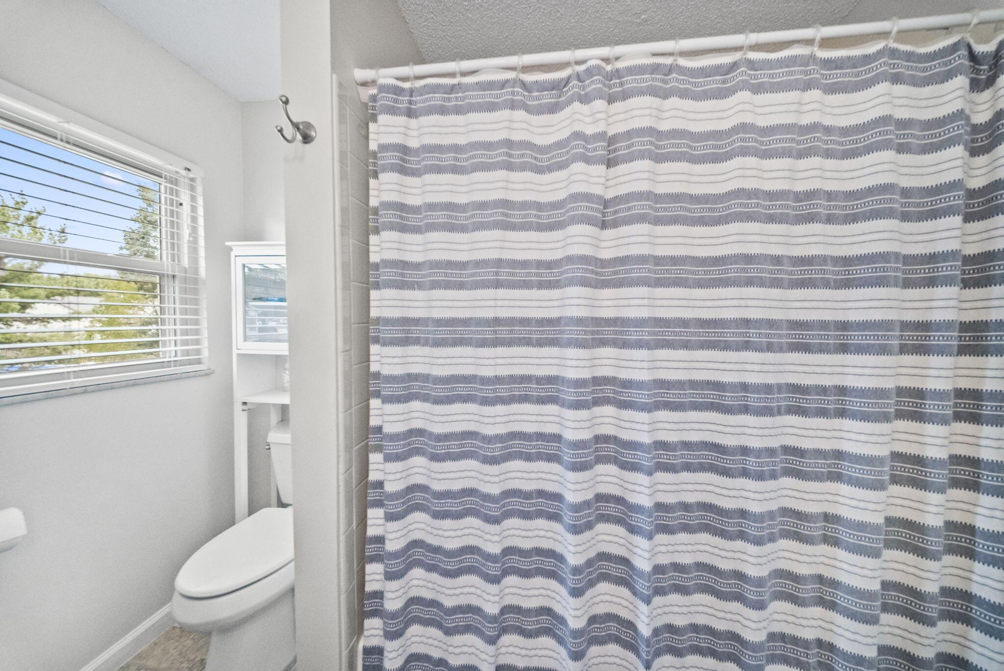 Bathroom with a striped shower curtain, toilet, and bright window.