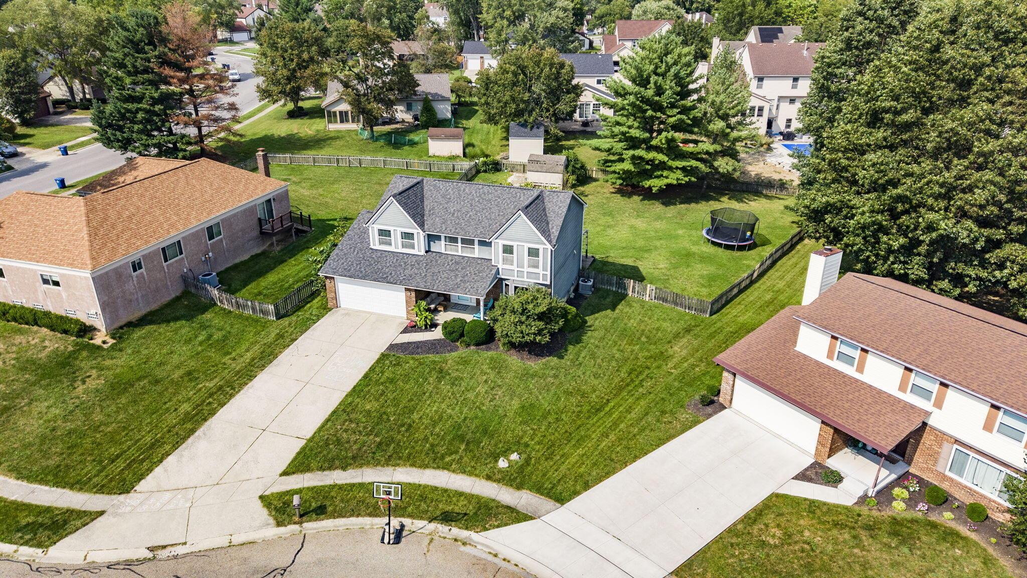 Aerial view of a two-story home with a fenced backyard, trampoline, and basketball hoop.