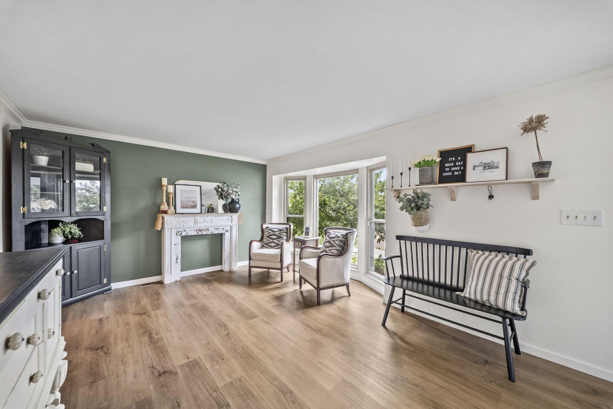 Staged living room with a white decorative fireplace, green accent wall, and tall windows.
