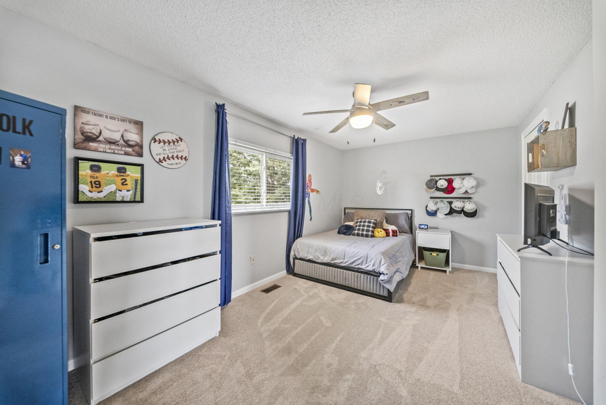 Bedroom with a gray bed, blue curtains, baseball decor, and rows of caps displayed on the wall.
