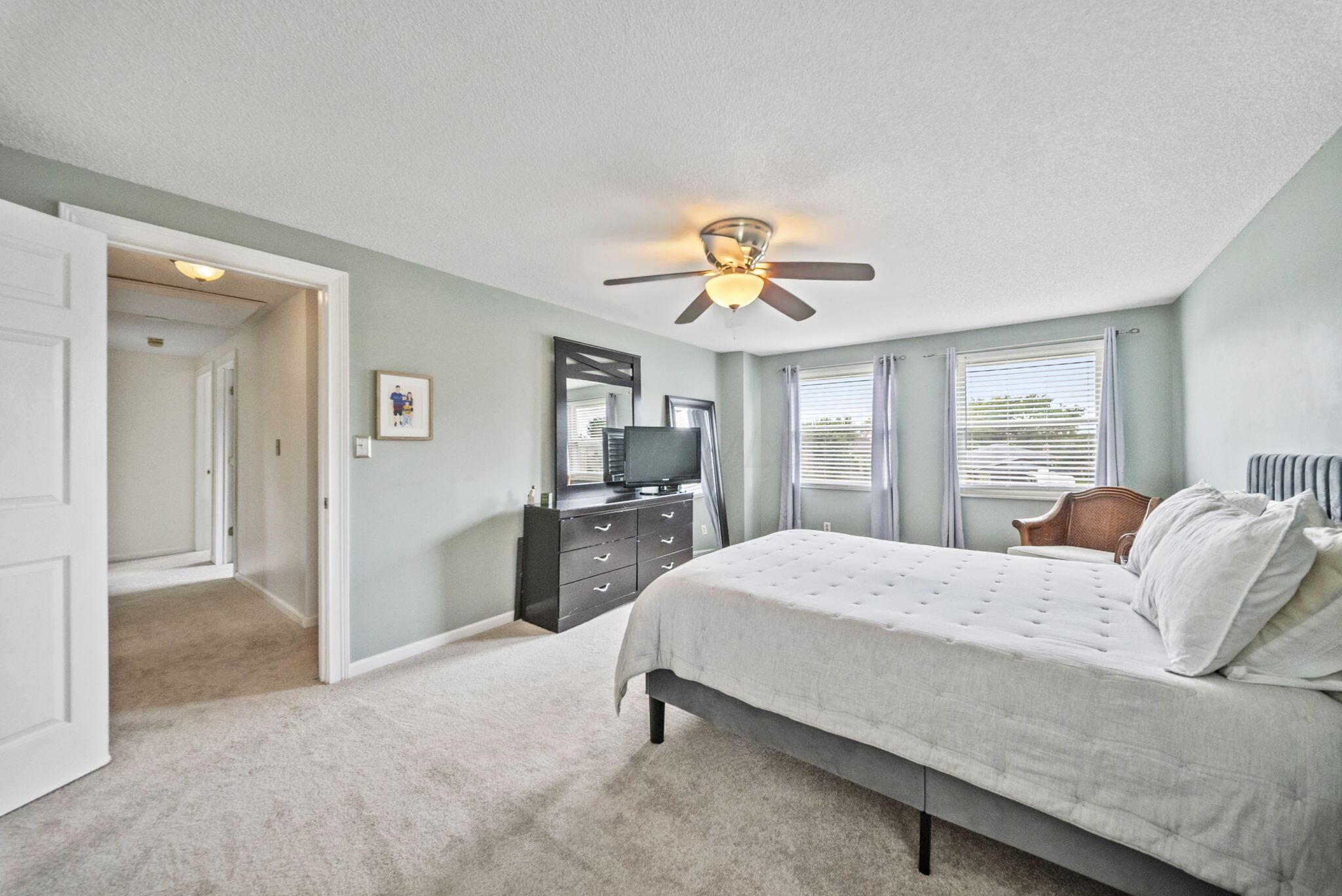 Bedroom with a large gray bed, ceiling fan, and two curtained windows.