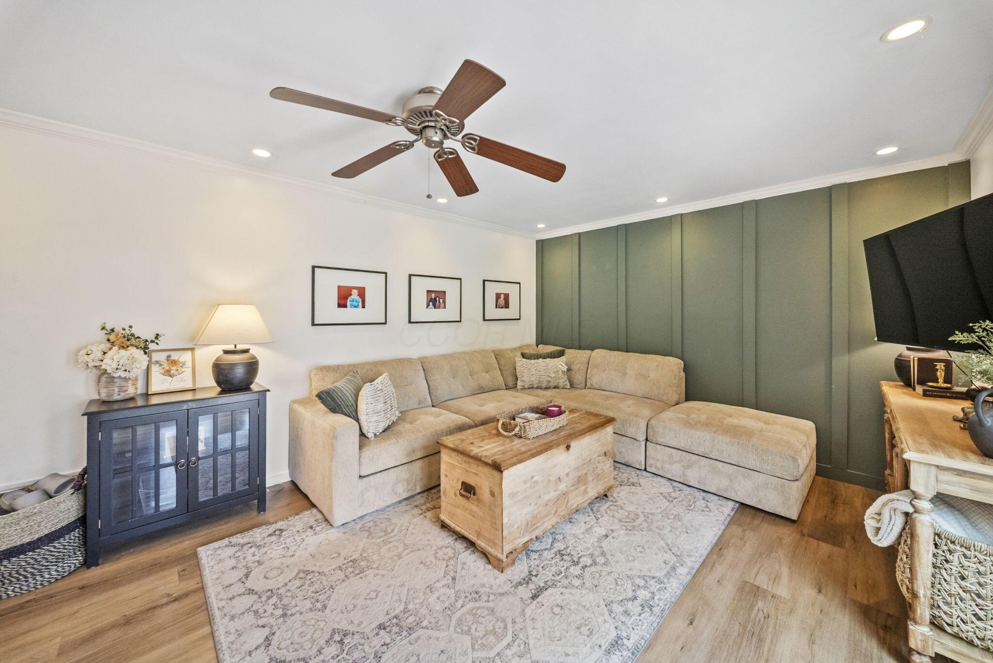 Living room with a beige sectional, green paneled accent wall, and wooden trunk coffee table.