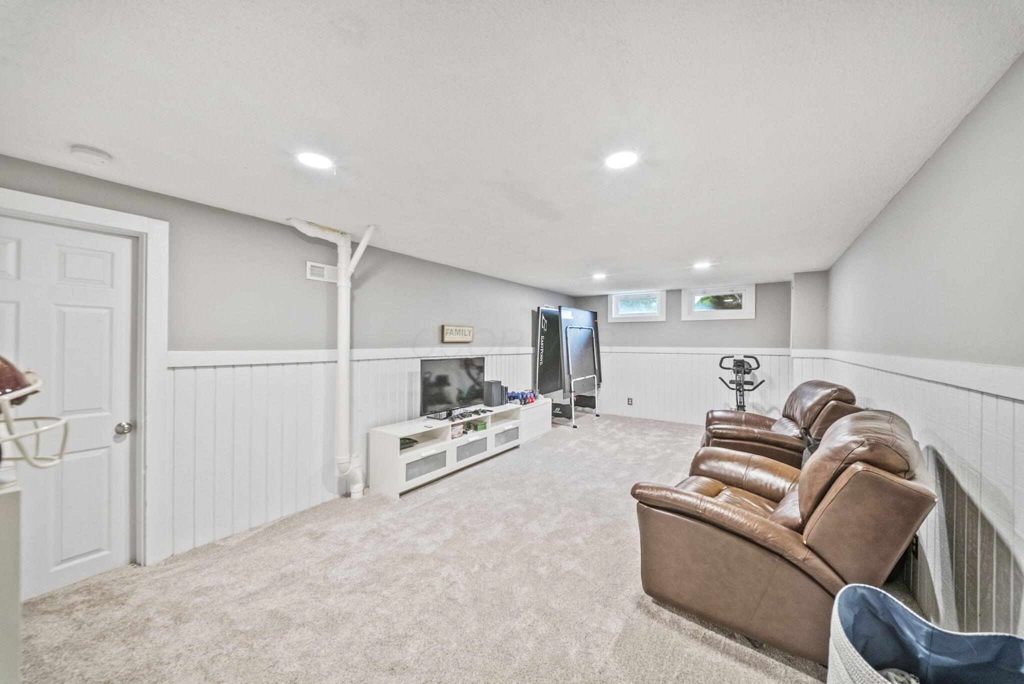 Basement family room with brown leather recliners, a TV, and exercise equipment.