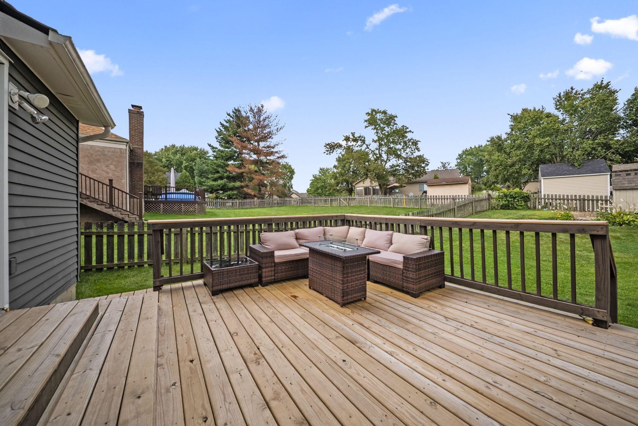 Wooden backyard deck with cushioned sectional seating and a fire table overlooking a fenced lawn.