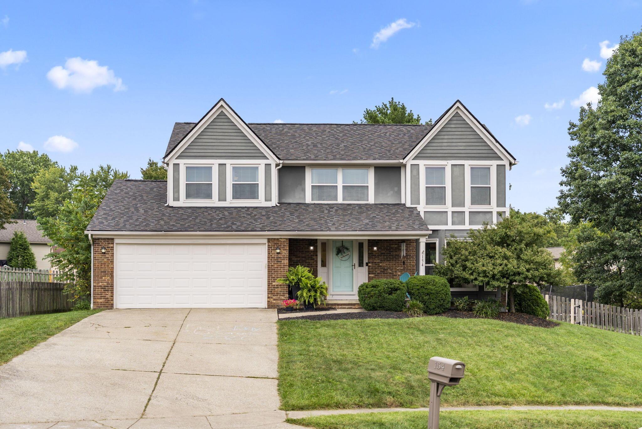Two-story gray-and-brick house with twin gables, a two-car garage, and a turquoise front door.