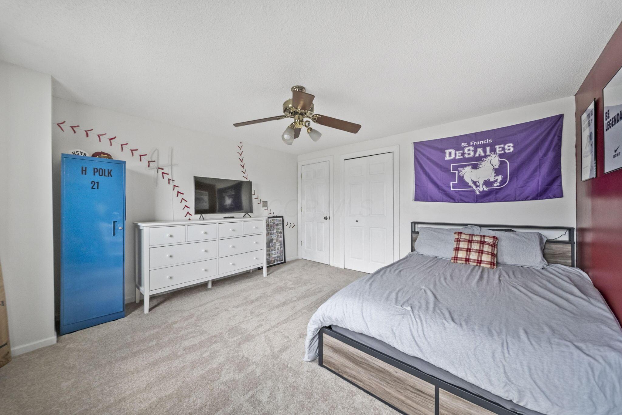 Bedroom with a gray bed, blue locker, white dresser, and purple St. Francis DeSales banner.