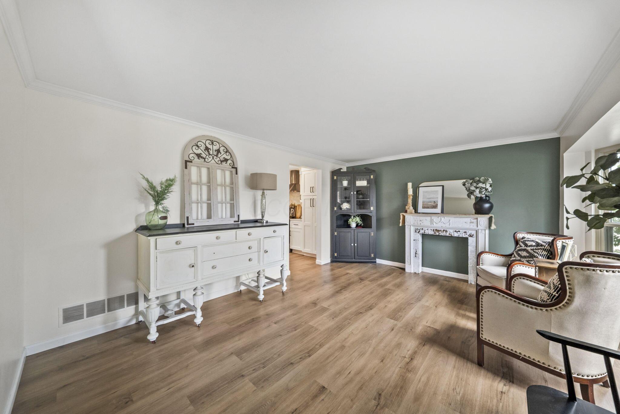 Living room with a white fireplace against a dark green wall and upholstered chairs.