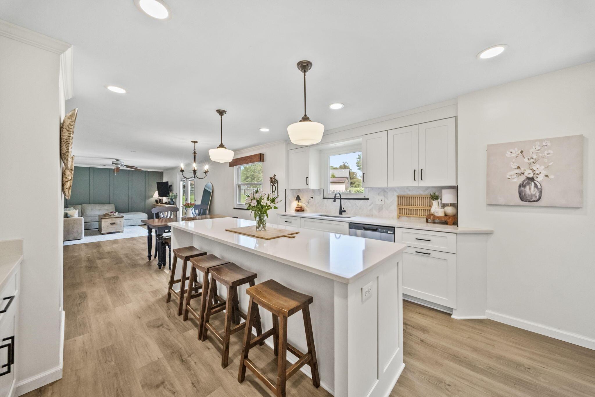 Open-plan kitchen with a large white island, wooden stools, and a living area beyond.