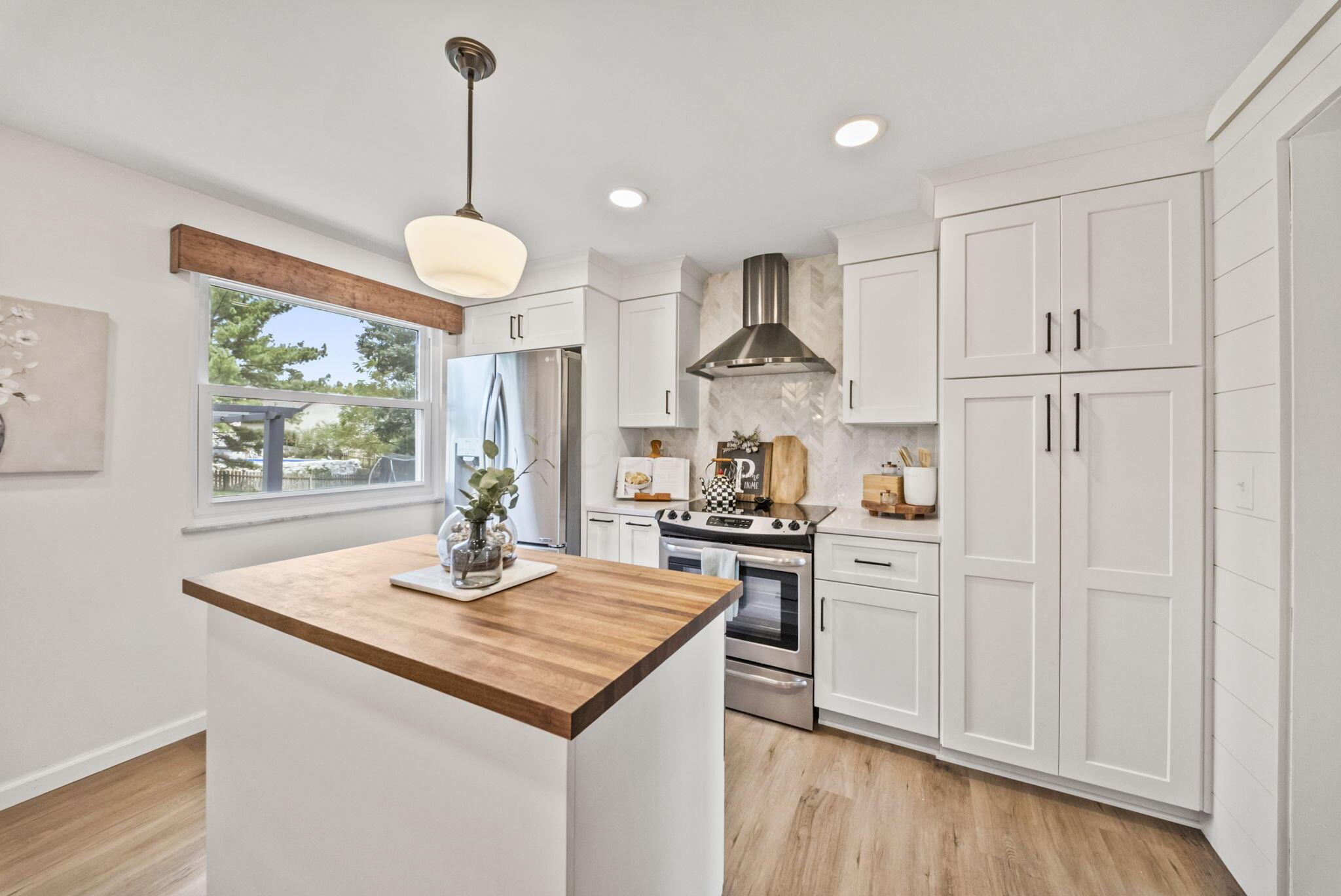 Bright kitchen with white cabinets, stainless steel appliances, patterned backsplash, and a butcher-block island.