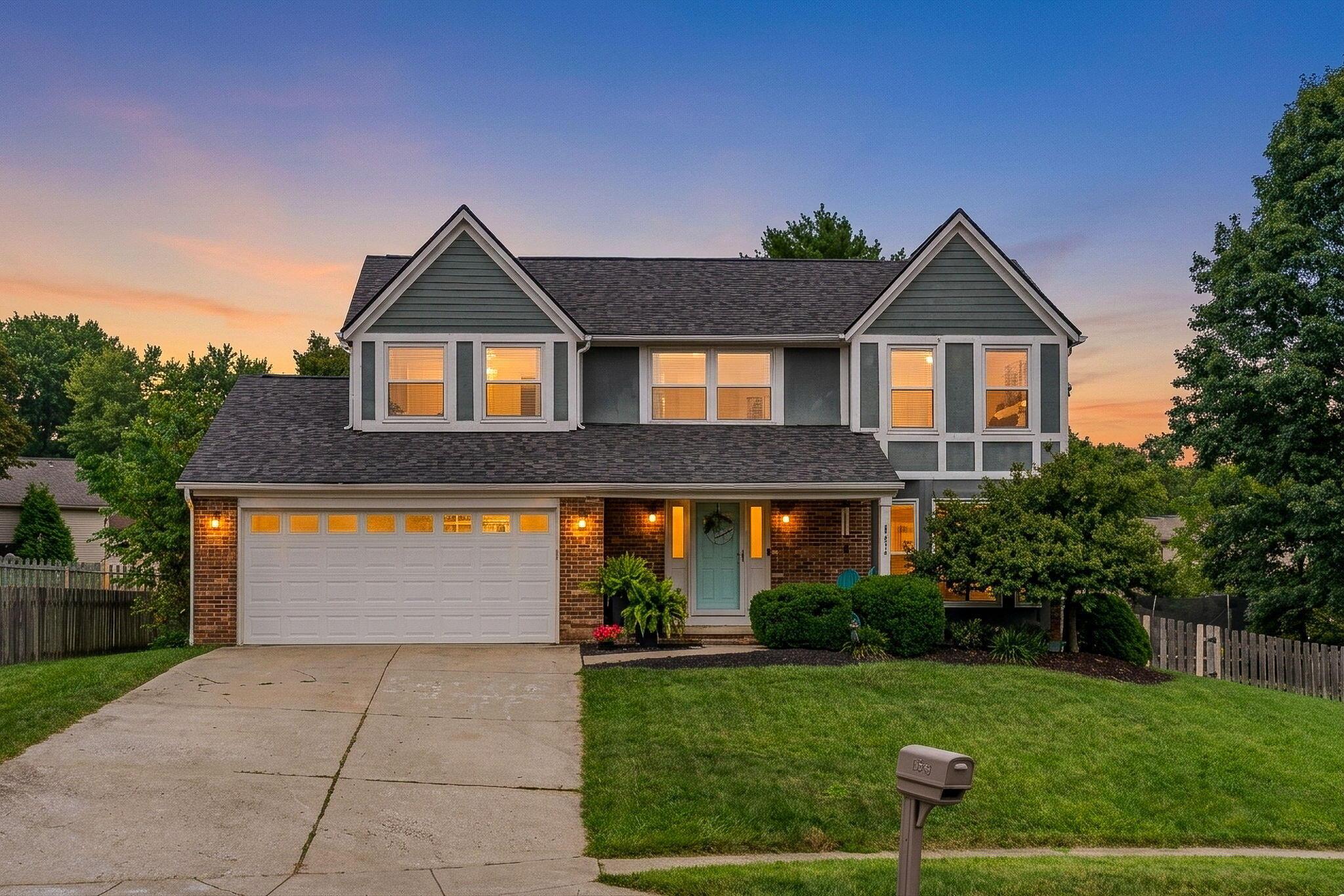 Two-story house with twin gables, brick lower facade, and a two-car garage at dusk.