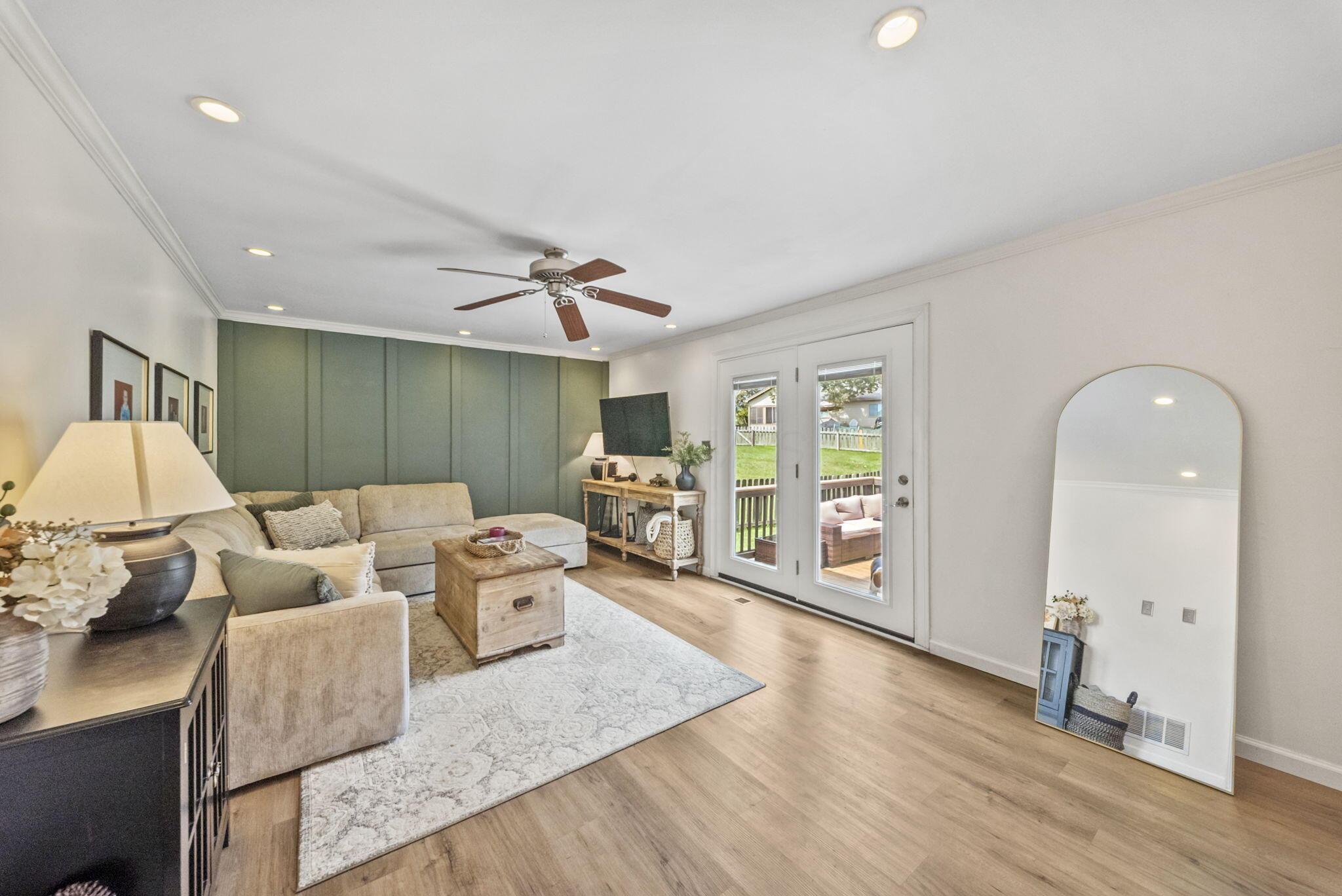 Staged living room with sage green paneled wall, beige sectional, and glass doors to the deck.