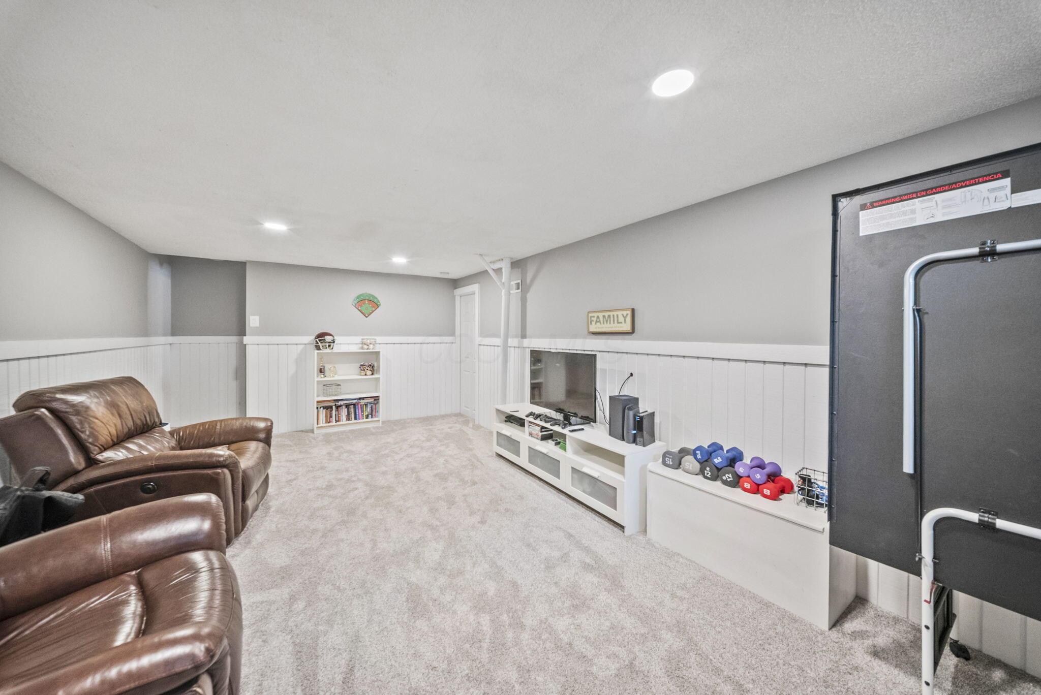 Basement recreation room with leather recliners, a television, and colorful dumbbells beside an exercise machine.