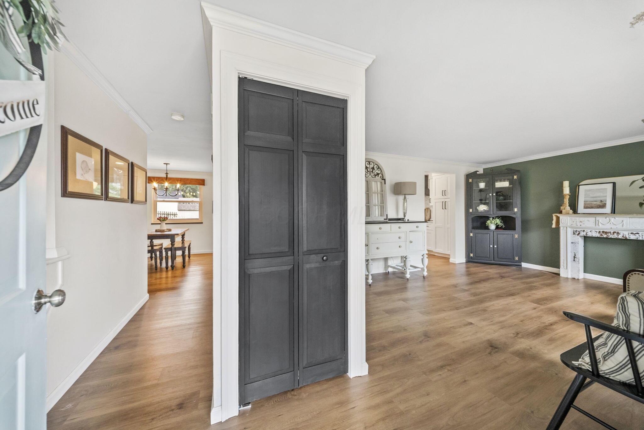 Living room with a green accent wall, white fireplace, wood floors, and charcoal paneled doors.