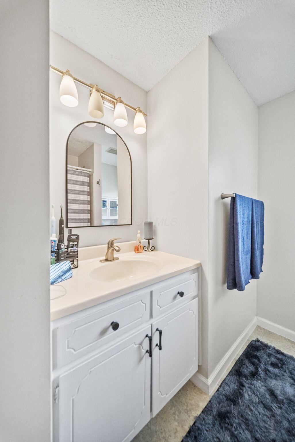 Bathroom vanity with an arched mirror, brass-toned lights, and blue towels.
