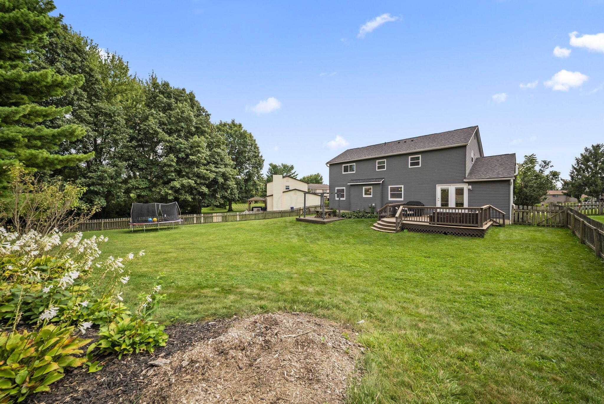 Gray two-story home with a raised deck overlooking a fenced lawn and trampoline.