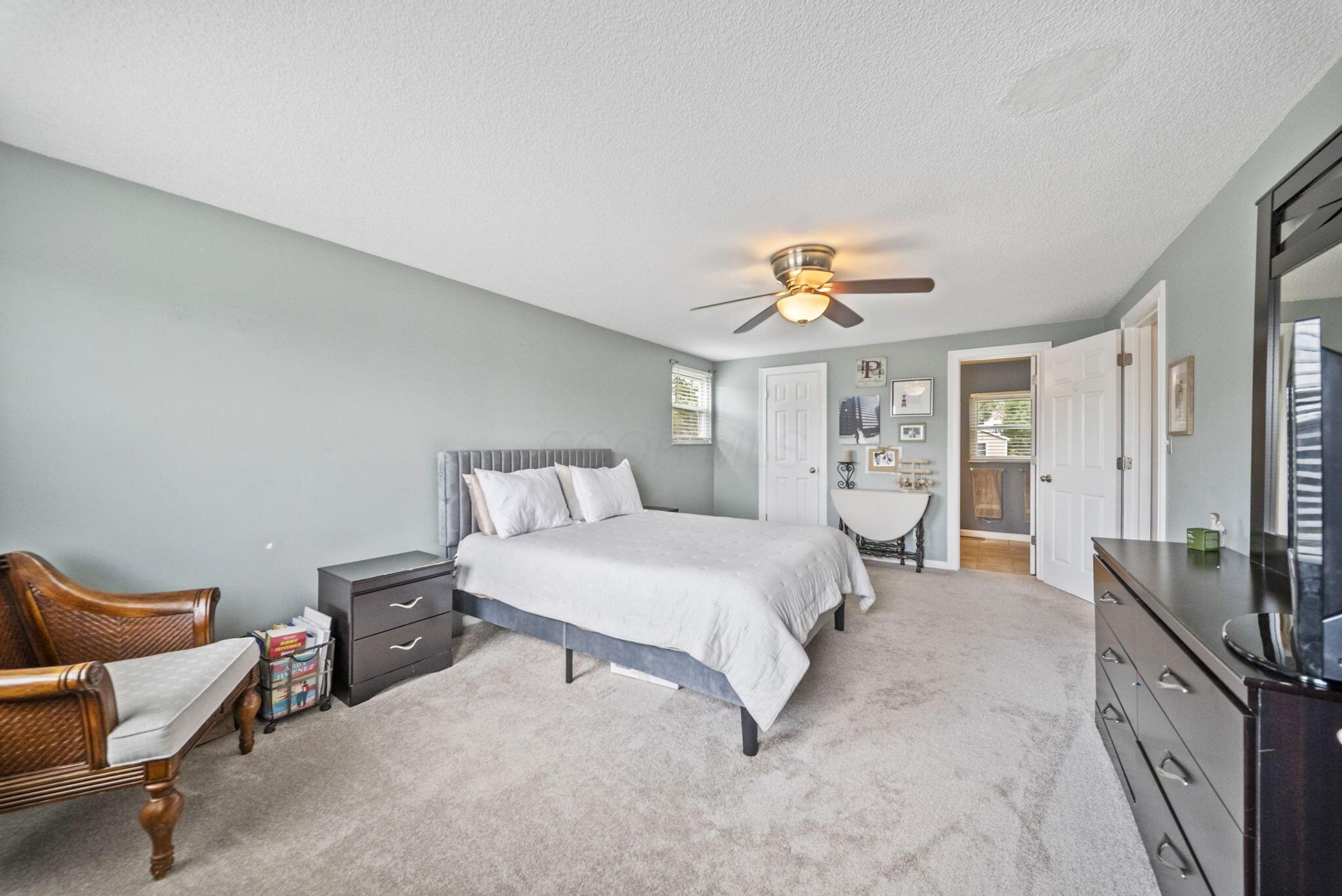 Furnished bedroom with a white bed, gray walls, ceiling fan, and wicker chair.