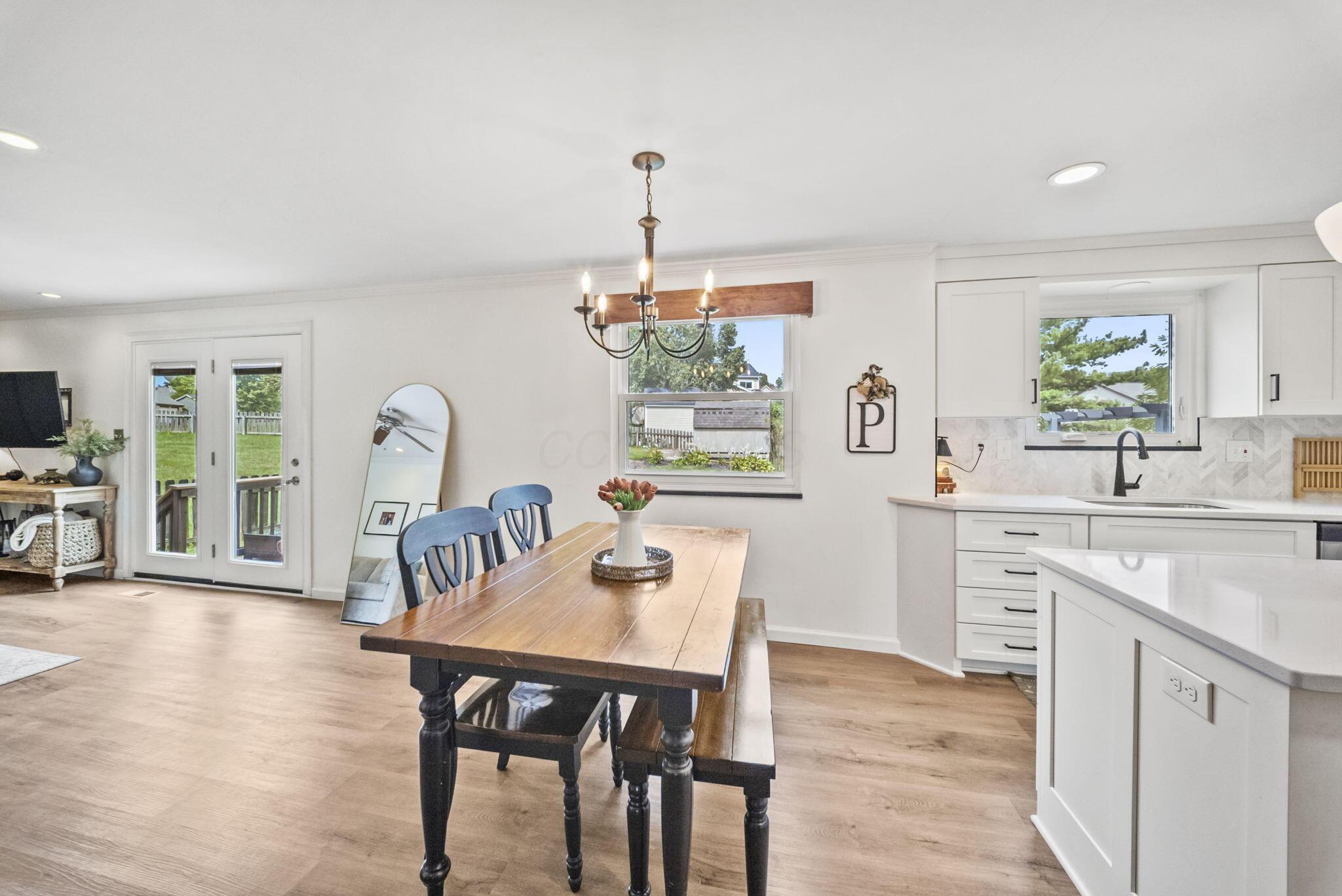 Bright kitchen and dining area with a large white island, wooden table, and backyard views.