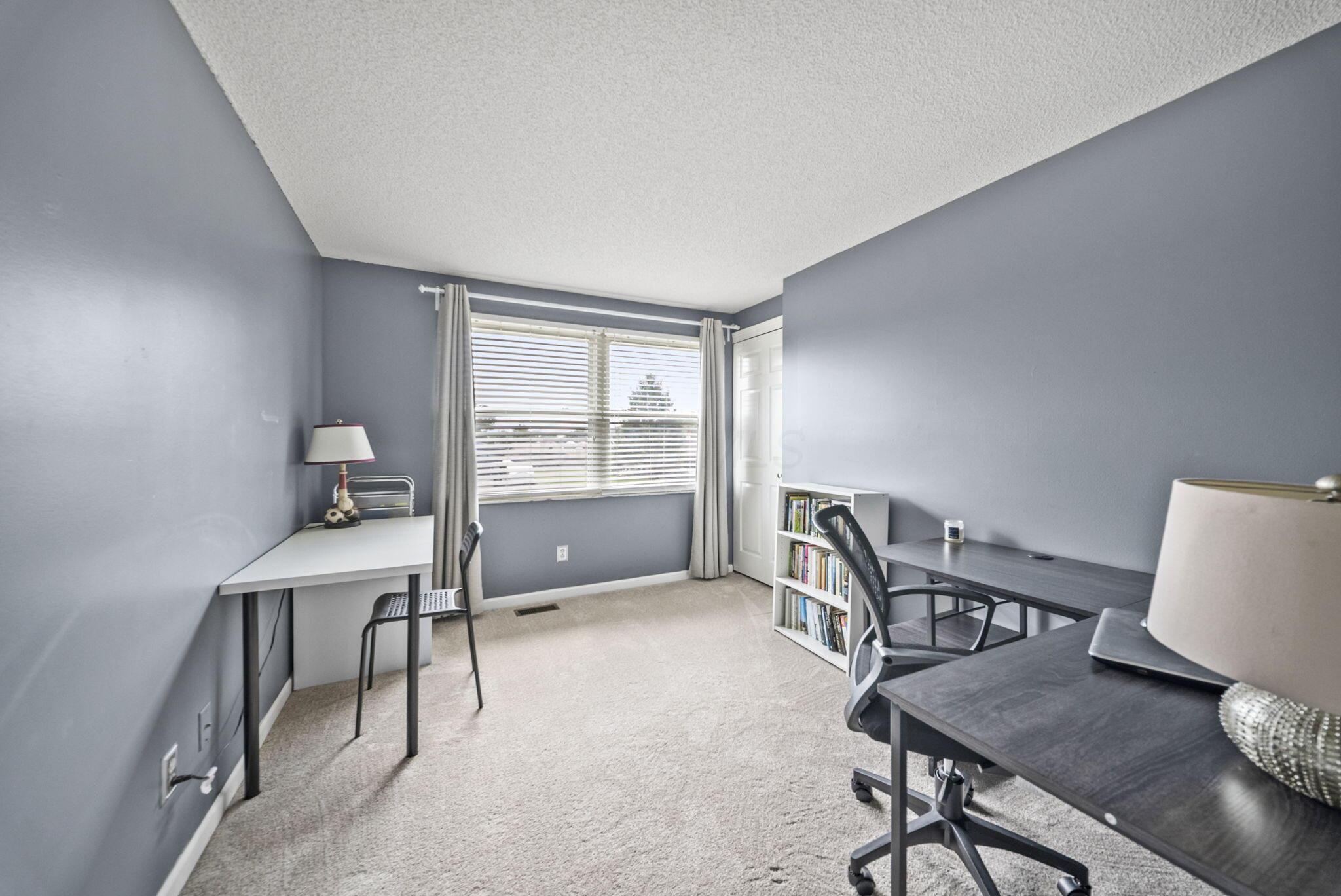 Home office with two desks and a large curtained window.