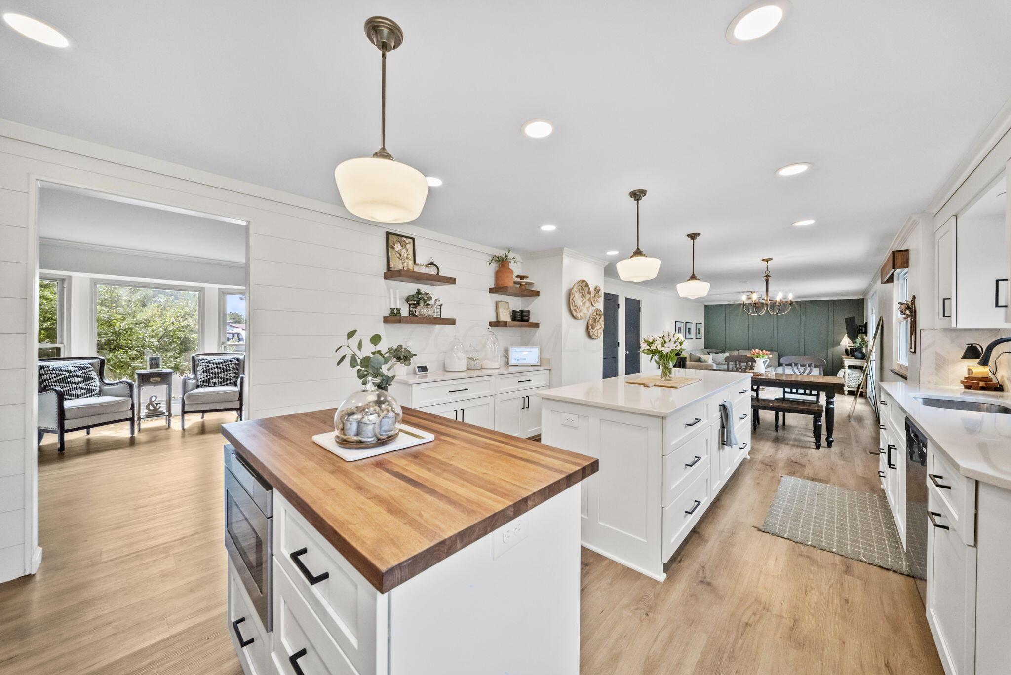Open-plan kitchen with white cabinetry, butcher-block island, and adjoining dining and living area.