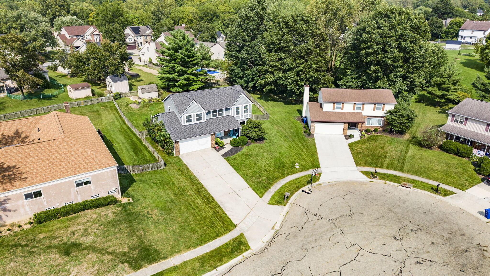 Aerial view of a two-story home with an attached garage, fenced yard, and mature trees.