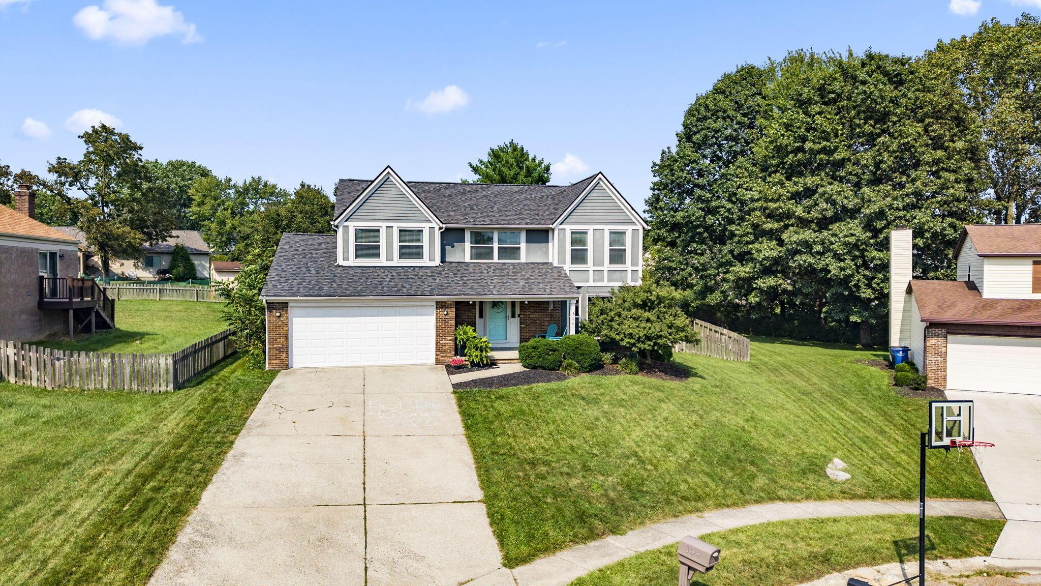 Two-story gray-and-brick house with a double garage, turquoise front door, and broad lawn.